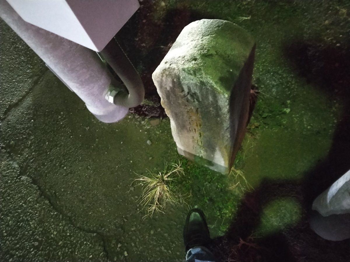 道路元標の横で撮影する人の足元と車道